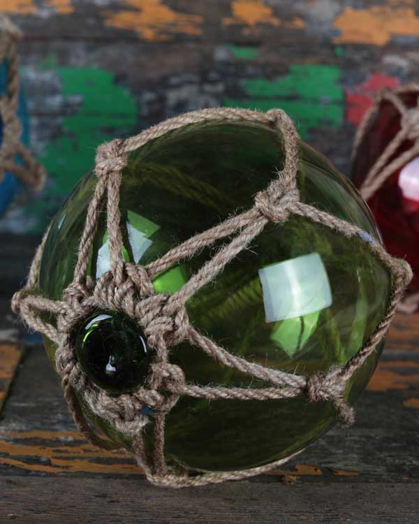 This is an image of a Fish Float in a Tiki Bar. The fish float is 20cm in diameter and green in colour and has a kotted jute rope net aound it with a hanging loop so that it can be used for decoration.
