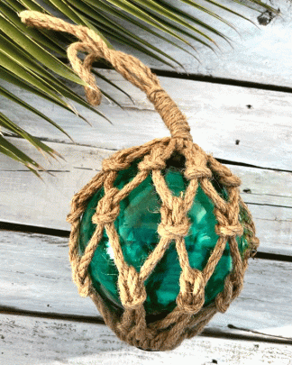 This is a photo of a glass fish float in aqua marine colour with chunky rope netting around the ball which is hanging on a white washed backdrop