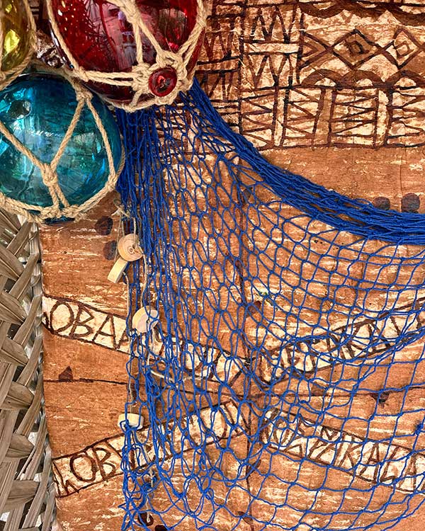 BLUE FISH NET WITH CORK FLOAT DETAIL HANGING ON A TAPA CLOTH WALL